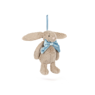 An image of a stark white background with a Jellycat Beige bunny in the center. The beige bunny has a velvet light blue bow at his collar and is affixed with a blue ribbon so it can be hung and used as decor.