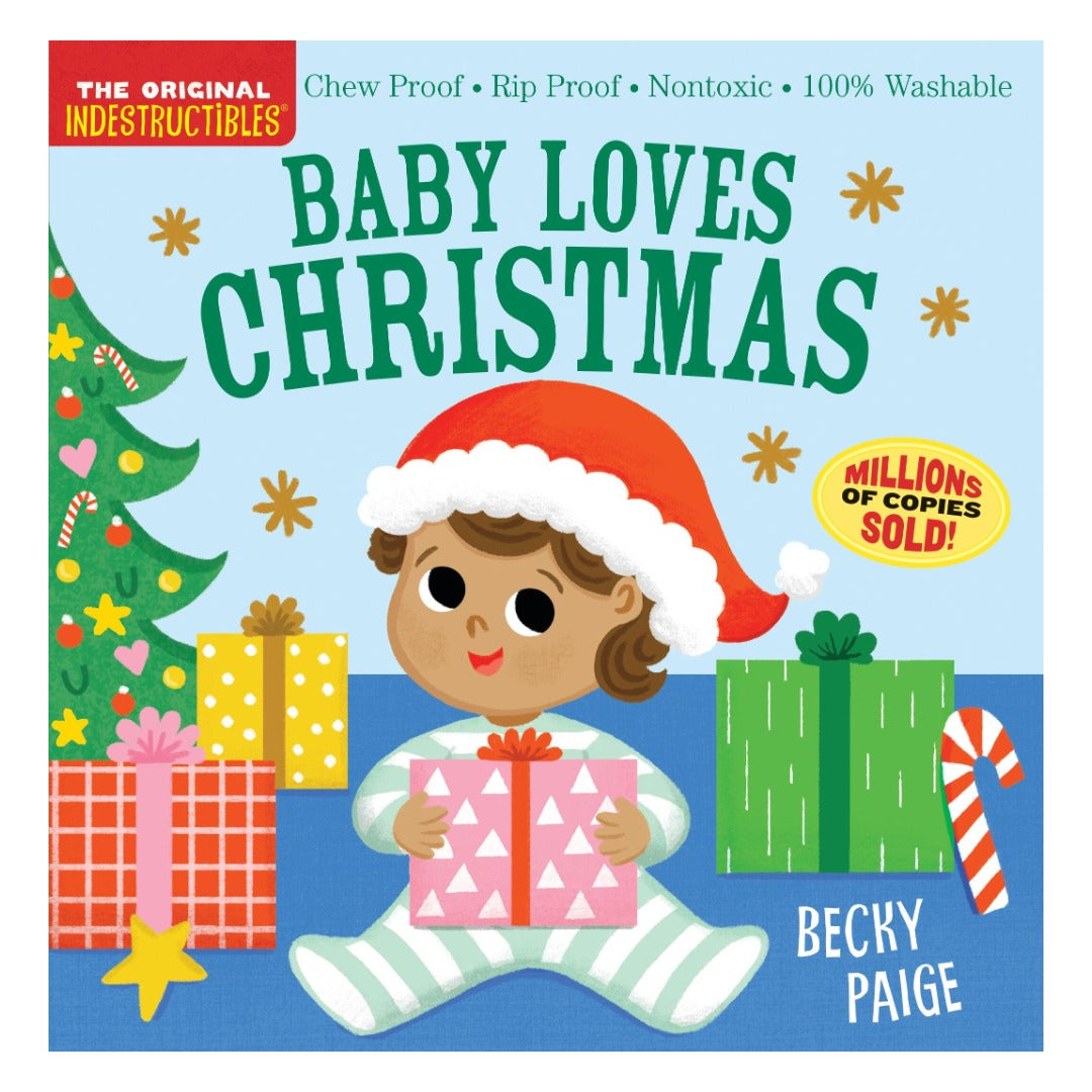 Cover of Indestructibles: Baby Loves Christmas, illustrated by Becky Paige, showing a baby in a red Santa hat holding a wrapped present beside a Christmas tree and a stack of gifts